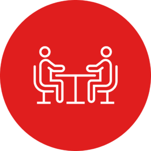 Icon showing two people sitting opposite each other at a desk.